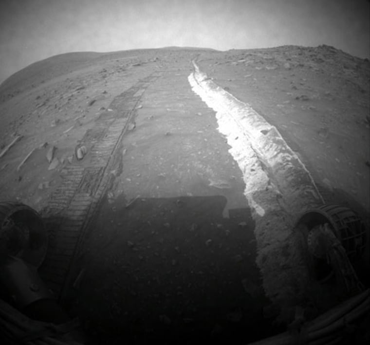 Spirit looks back at its tracks on Sol 1861 of its mission on Mars. Its immobile right-front wheel, which forces the rover to drive backwards, churned up bright soil. The edge of Home Plate forms the horizon on the right side of this image. Husband Hill is on the horizon on the left side. The parallel rover wheel tracks are about 40 inches apart. 
